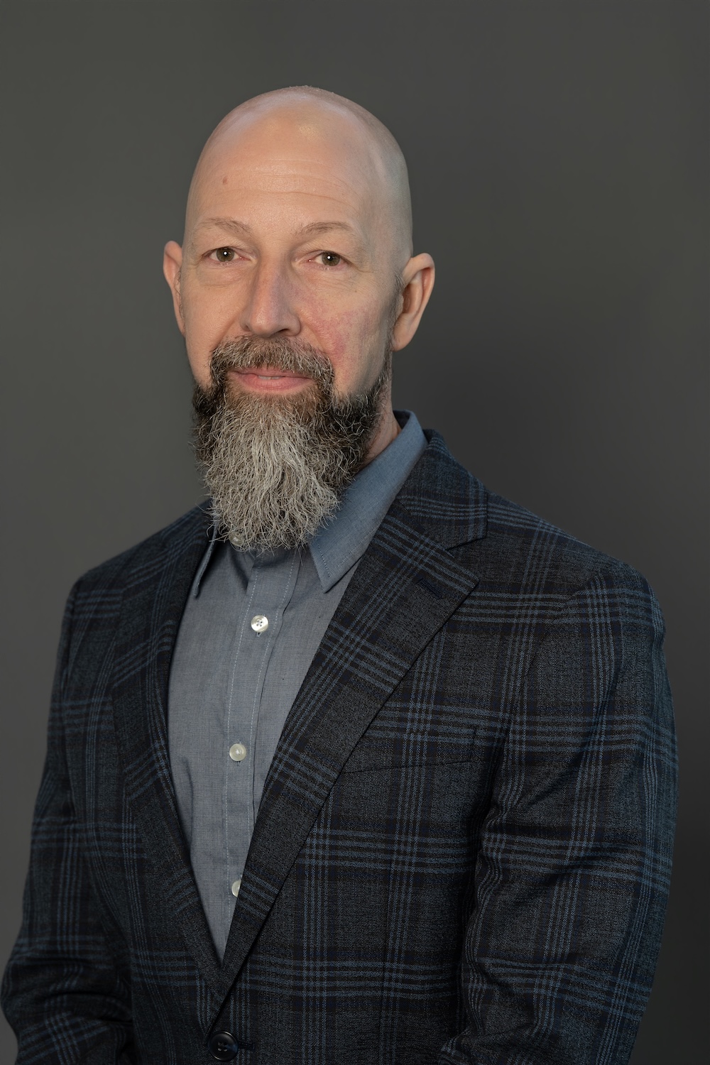 Head-and-shoulders portrait of a bald man with a gray beard in a blue shirt and navy plaid blazer.