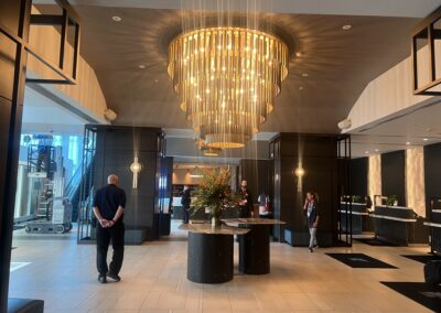 Luxurious hotel lobby with a multi-tier gold chandelier hanging overhead and guests at a dark reception area.