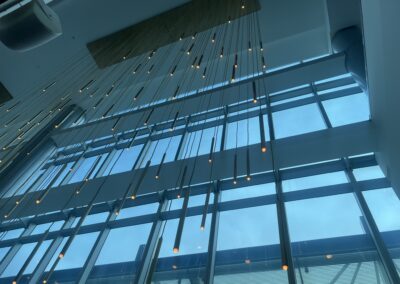 Modern glass atrium with numerous vertical pendant lights hanging from the ceiling against blue-tinted windows.