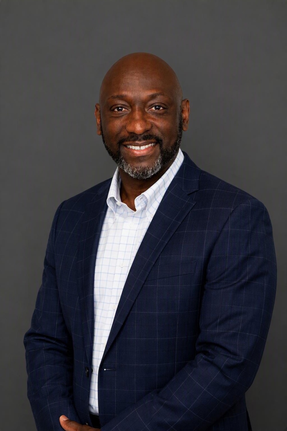 Anthony-Sparkling_E+Headshot_Updated Smiling Black man in a navy checkered blazer and white shirt against a gray backdrop.