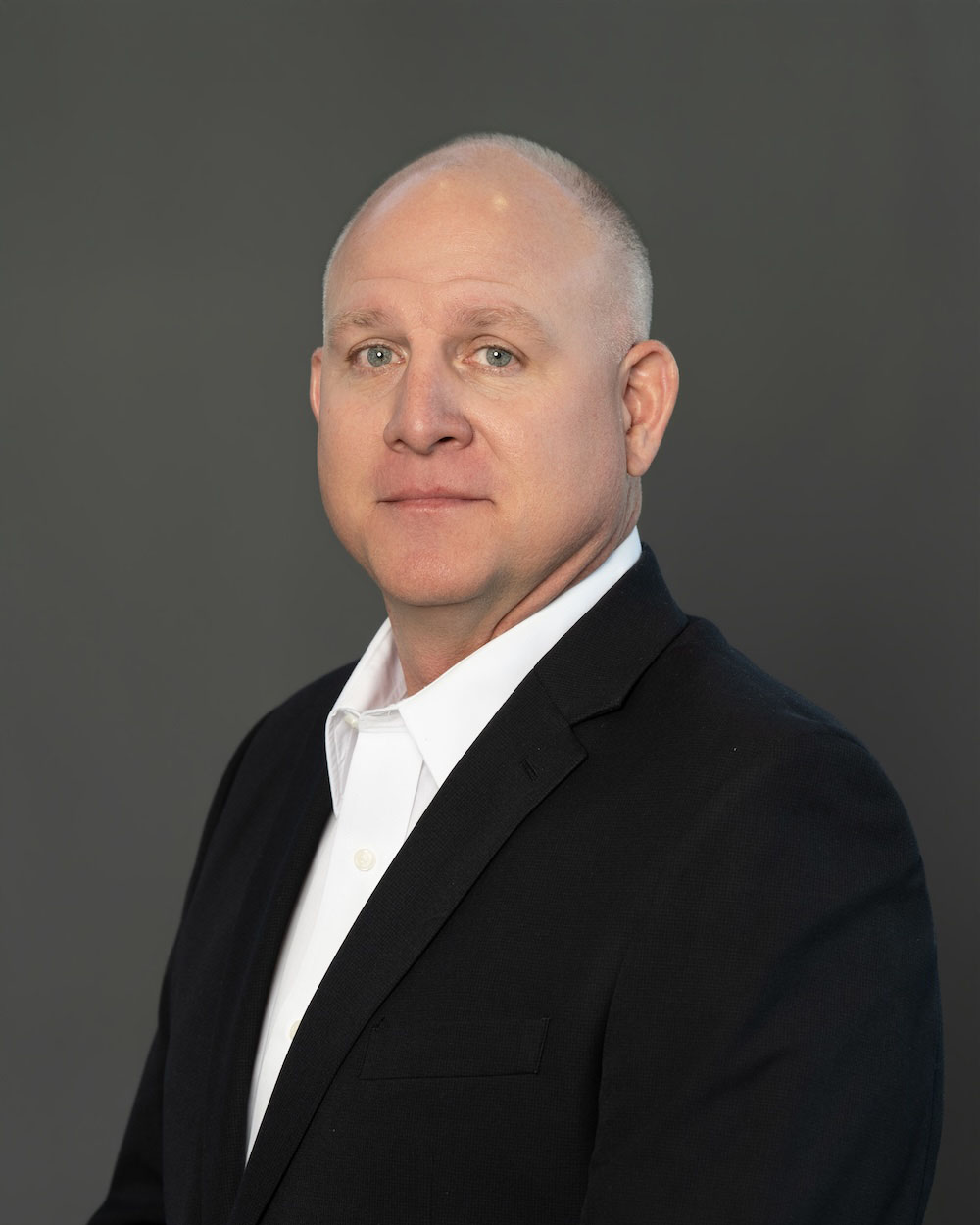 Steve-Webb-edit-2 Professional headshot of a bald man in a black suit and white shirt, looking at the camera against a gray backdrop.